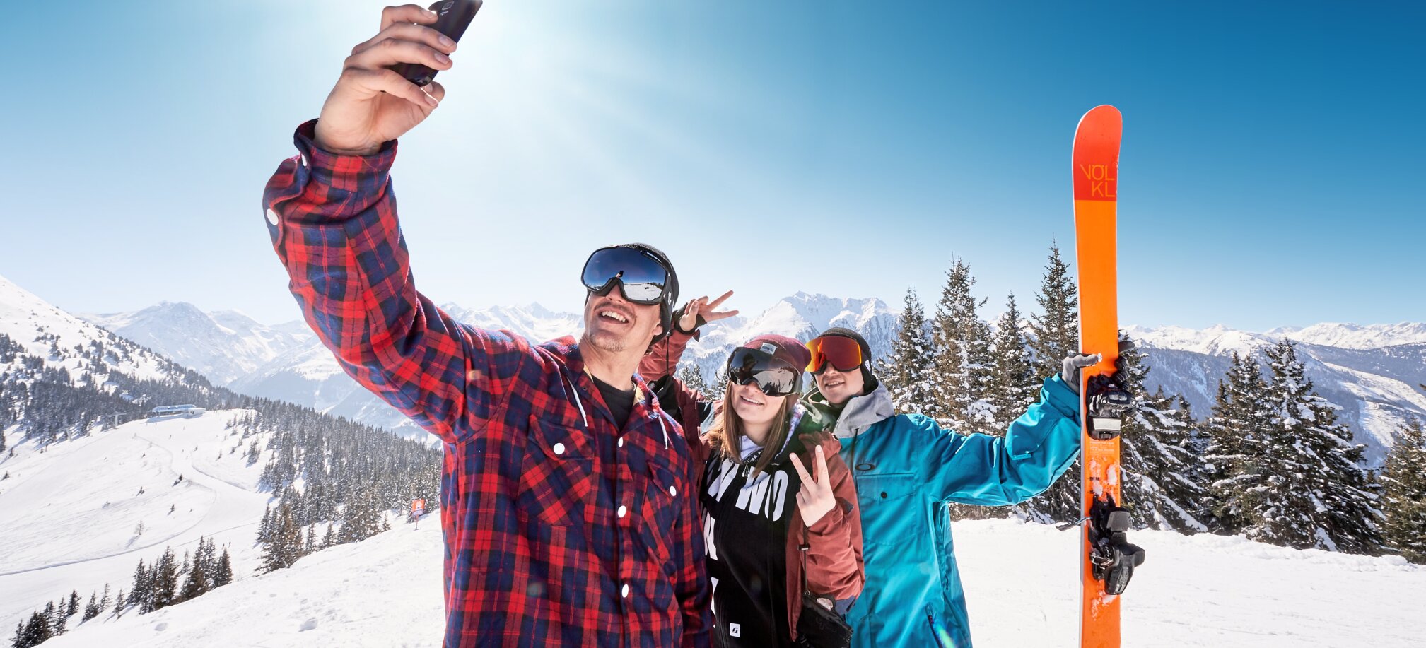 Three youthful skiers pose for a selfie in front of a snow-covered mountain landscape. | © Ski amadé