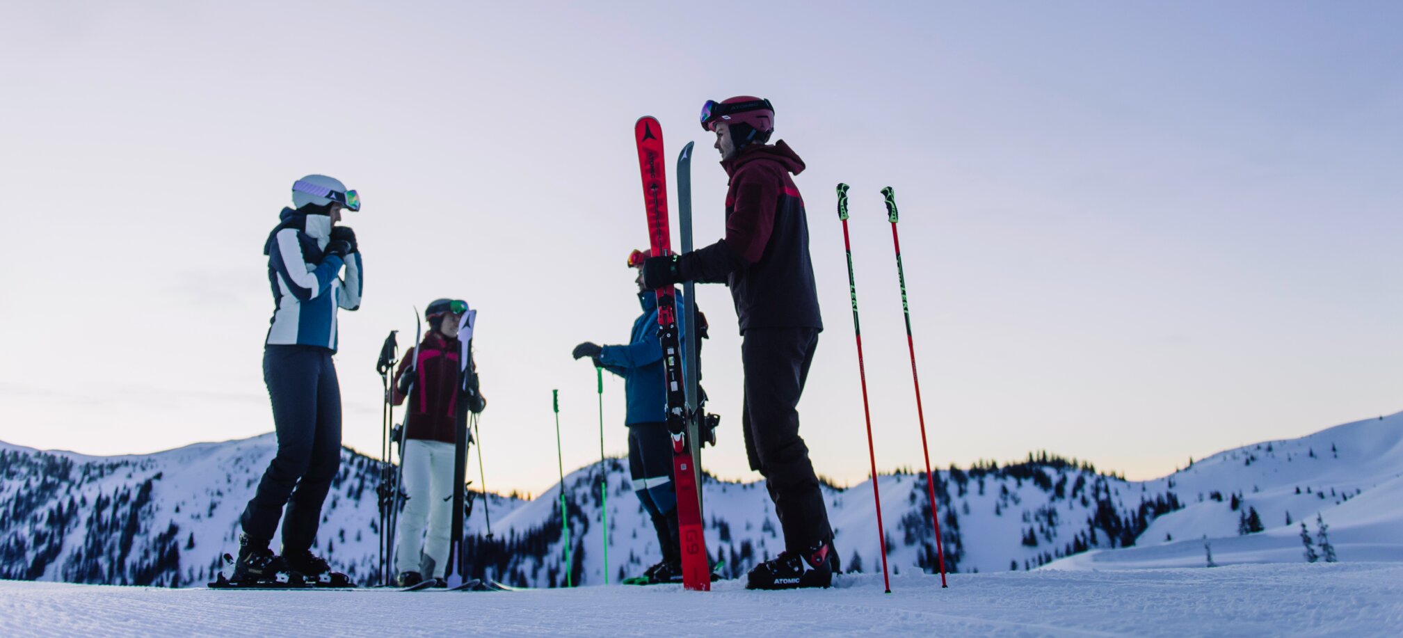Vier Skifahrer stehen auf einem verschneiten Hang unter einem violetten Himmel. | © Ski amadé
