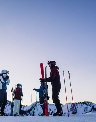 Four skiers stand on a snowy slope under a violet sky. | © Ski amadé