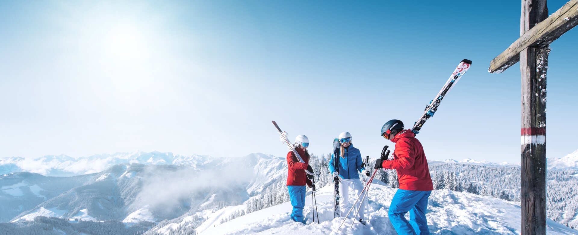 Drei Skifahrer stehen an einem Gipfelkreuz und genießen die Berglandschaft. | © Ski amadé