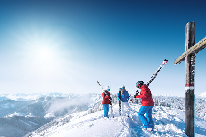 Sensational views while skiing | © Ski amadé Three skiers stand by a summit cross, enjoying the mountain scenery. | © Ski amadé
