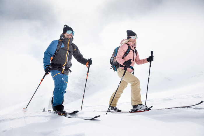 Dirndl ski tour ascending through fresh powder snow | © Harald Steiner Two ski tourers ascend side by side through fresh snow under a cloudy alpine sky | © Harald Steiner