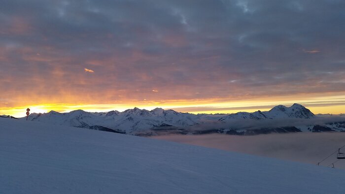 Skitour Dorfgastein Mittelstation bei Sonnenaufgang Verschneite Berghänge mit orangefarbenem Sonnenaufgang und Wolken über Mittelstation