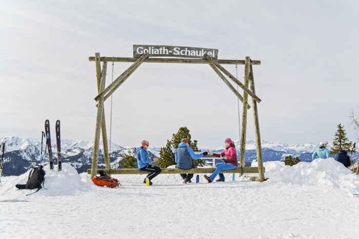 Goliath-Schaukel auf der Fageralm – Rastpunkt bei Skitour Skitourengeher sitzen auf großer Holzschaukel mit Ausblick auf verschneite Bergwelt