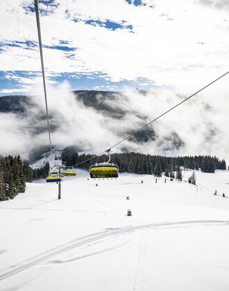 Gelber Sessellift fährt über verschneite Pisten und Wald in nebeliger Winterlandschaft | © filzmoos.ski
