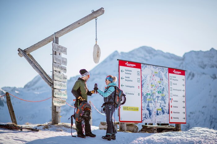 Zwei Tourenskigeher an einer Wetterstation in den Bergen | © Christoph Huber Zwei Wintersportler stehen an einer Wetterstation mit Holzschild in den Bergen und studieren eine große Pistenkarte. | © Christoph Huber