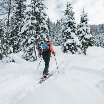 Skitourengeher mit Rucksack geht durch tief verschneiten Nadelwald in unberührtem Schnee | © Gasteinertal Tourismus GmbH, Christoph Oberschneider