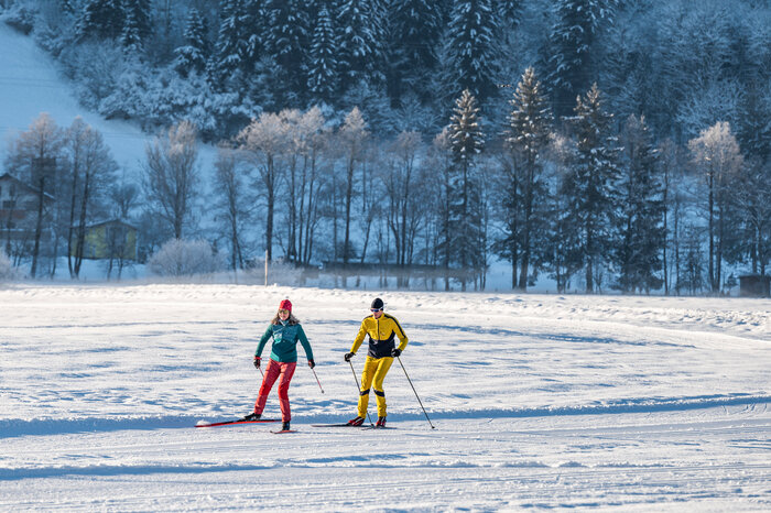 Two cross-country skiers on groomed trail in winter landscape with snowy trees in the background | © Salzburger_Sportwelt_Lorenz_Masser