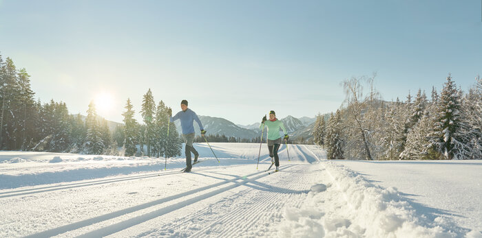 Langlaufen in der Ramsau | © Peter Burgstaller Zwei Langläufer laufen auf einer sonnenbeschienenen Loipe | © Peter Burgstaller