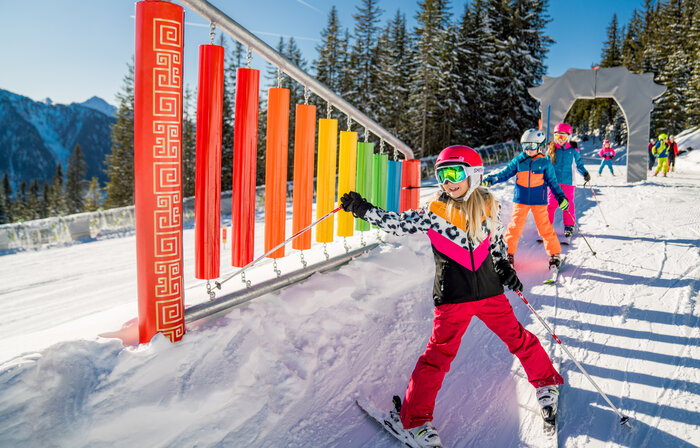 Winterkinderland Planai | © Christine Höflehner Kind fährt mit Ski an bunten Klangstäben vorbei und hält den Skistock auf die Stäbe, um einen Klang zu erzeugen | © Christine Höflehner