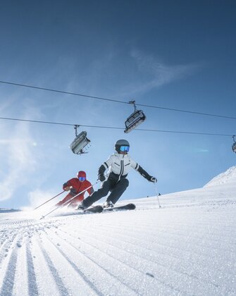 Two skiers carving beneath lift in bright mountain sun