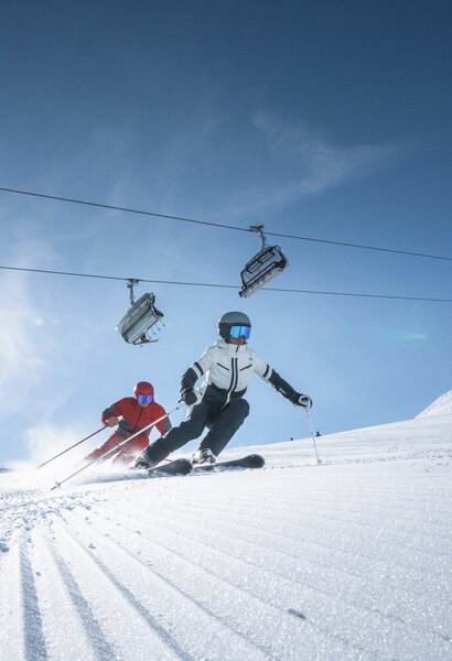 Two skiers carving beneath lift in bright mountain sun