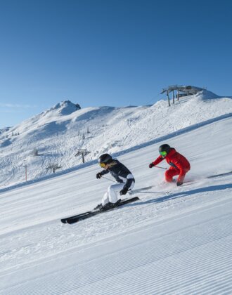 Skifahren mit atemberaubender Bergkulisse | © Zwei Skifahrer gleiten elegant über frisch präparierte Pisten mit beeindruckendem Panorama in Ski amadé. Perfekte Bedingungen für unvergessliche Skitage.