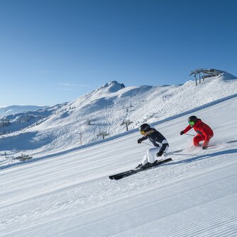 Skifahren mit atemberaubender Bergkulisse | © Zwei Skifahrer gleiten elegant über frisch präparierte Pisten mit beeindruckendem Panorama in Ski amadé. Perfekte Bedingungen für unvergessliche Skitage.