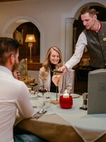Kellner serviert einem Paar mit Rotwein das Abendessen am festlich gedeckten Tisch | © Nadia Jabli