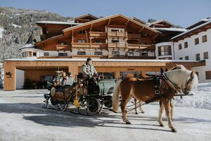 Pferdeschlitten mit Fahrer und Gästen vor dem verschneiten Hotel Tauernhof