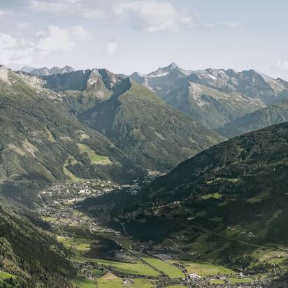 Wide view over Gastein Valley with a town below, green slopes and a long mountain range under a bright sky. | © Gasteinertal Tourismus, Marktl Photography