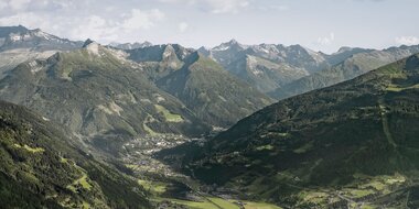 Weitblick über das Gasteinertal mit Ort im Tal, grünen Hängen und einer langen Bergkette unter hellem Himmel. | © Gasteinertal Tourismus, Marktl Photography
