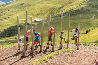 Several kids balancing on wooden posts at Schlossalm children's area with alpine summer backdrop and green hills | © Gasteiner Bergbahnen AG