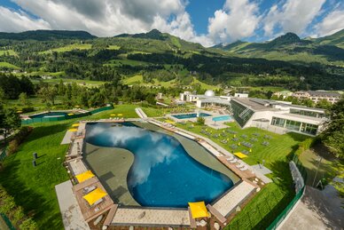 View of Alpentherme Gastein with large thermal lake, sunbathing lawns and surrounding mountain scenery in summer | © Alpentherme Gastein, Wolkersdorfer