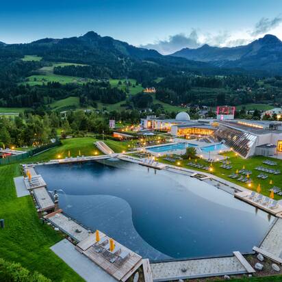 Evening view of Alpentherme Gastein with illuminated bathing lake and green mountain scenery in the background
