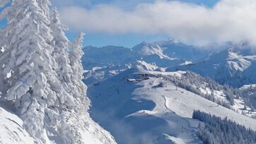 Sicht auf eine Bergstation von einem Sessellift und ein Piste umrahmt von einer tiefverschneiten Berglandschaft