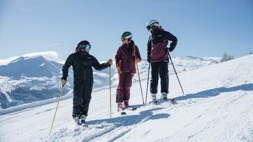 Drei Personen in Skiausrüstung stehen auf einer Piste und unterhalten sich lächelnd | © Gasteinertal Tourismus GmbH, Christoph Oberschneider