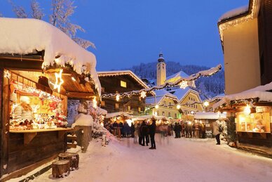Beleuchtete Adventstände beim Salzburger Bergadvent in Großarl mit Besuchern, Kirche und verschneiten Häusern | © Tourismusverband Großarltal