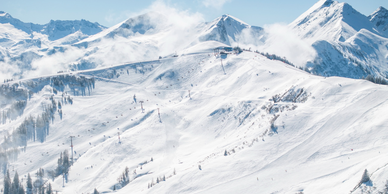 Weite Ansicht des Skigebiets Großarltal mit präparierten Pisten, Liften, verschneiten Gipfeln und aufziehenden Wolken | © Lorenz Masser
