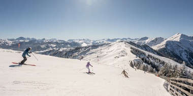 Three skiers descend a wide groomed slope in Grossarltal ski area with snowy mountains under bright sun | © Lorenz Masser
