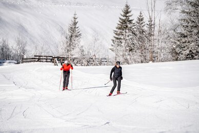 Zwei Langläufer auf präparierter Loipe im Großarltal mit verschneiten Wiesen, Bäumen und Winterlandschaft | © Gipfelfieber