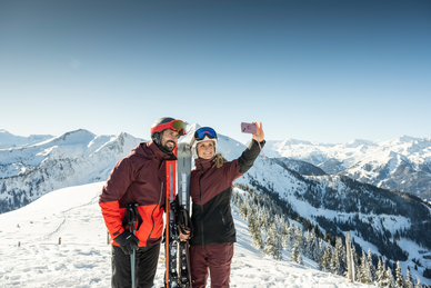 Paar in Skikleidung macht Selfie mit Smartphone vor verschneiter Bergkulisse im Skigebiet Großarltal | © TVB Großarltal - Lorenz Masser