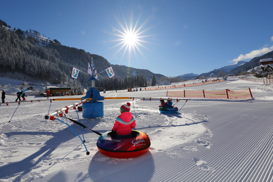 Kinder fahren mit Reifenkarussell auf der verschneiten Erlebniswiese im Großarltal bei Sonnenschein
