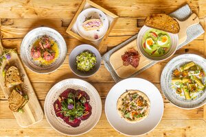 Mehrere angerichtete Speisen mit Brot, Suppe, Salat und Dessert liegen auf einem rustikalen Holztisch. | © Hochkönig Tourismus GmbH