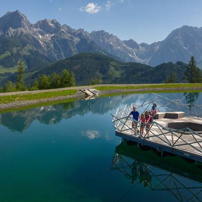 Familie auf Holzplattform am Prinzensee in Maria Alm, klares Wasser, Bergpanorama Hochkönig im Hintergrund | © Roland Haschka