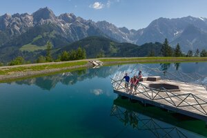 Family on wooden platform at Prinzensee in Maria Alm, clear lake water and Hochkönig mountains in background | © Roland Haschka