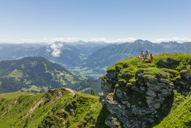 Familie sitzt auf einem Felsvorsprung und rundherum sind hohe Berge zu sehen | © Roland Haschka