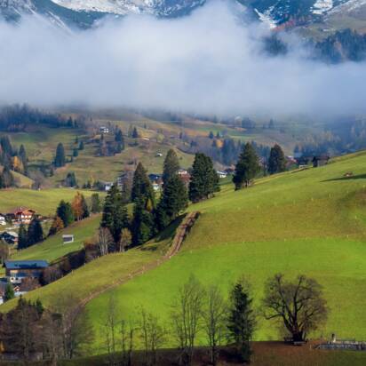 White church near Dienten on green hill, snowy Hochkönig rises above misty valley in the background