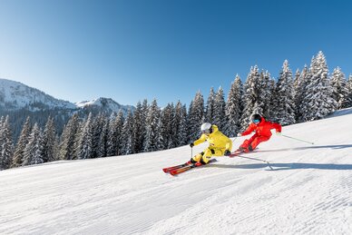 Two skiers in yellow and red outfits skiing in parallel on a snowy slope | © Hochkönig Tourimus GmbH