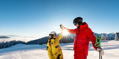 Two skiers in yellow and red gear give each other a high five on ski slope | © Hochkönig Tourismus GmbH