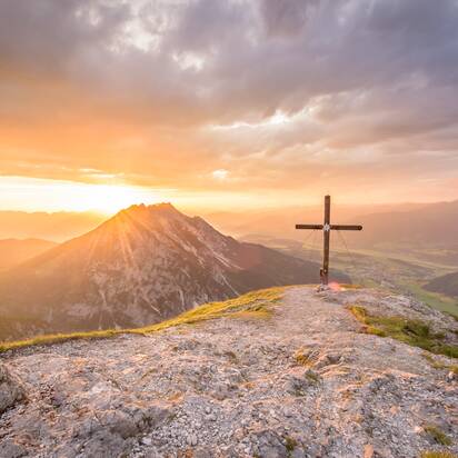 Gipfelkreuz bei Sonnenaufgang mit Blick über das Gröbminger Land, Berglandschaft in goldenes Morgenlicht getaucht | © Christoph Huber