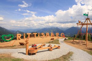 Panorama-Spielplatz mit Holzbuchstaben, Schaukeln und Wasserspiel vor Bergkulisse am Rittisberg | © Photo Austria, Hans-Peter Steiner