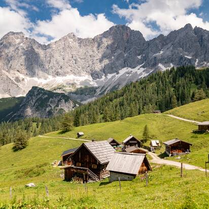 Traditionelle Almhütten der Neustattalmen vor saftig grünen Wiesen und dem markanten Dachsteinmassiv in Ramsau | © Schladming-Dachstein