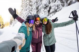 Drei Skifahrerinnen posieren lachend für ein Selfie auf einer verschneiten Piste | © Mirja Geh
