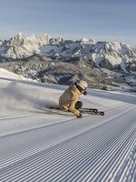 Skifahrer zieht eine tiefe Kurve auf frisch präparierter Piste mit Bergpanorama | © Mirja Geh