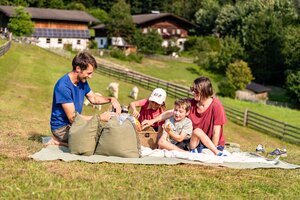 Family enjoying summer picnic on green meadow with farmhouses and grazing pasture in background | © TVB Eben