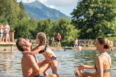 Familie beim fröhlichen Baden im Natursee mit Bergen und Badegästen im Hintergrund | © TVB Eben, Lorenz Masser