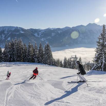 Eine Familie fährt die Piste hinunter und das Tal ist von Nebel bedeckt, während oben ein strahlend blauer Himmel zu sehen ist | © Michael Grössinger