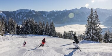 Eine Familie fährt die Piste hinunter und das Tal ist von Nebel bedeckt, während oben ein strahlend blauer Himmel zu sehen ist | © Michael Grössinger