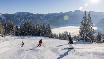 Eine Familie fährt die Piste hinunter und das Tal ist von Nebel bedeckt, während oben ein strahlend blauer Himmel zu sehen ist | © Michael Grössinger